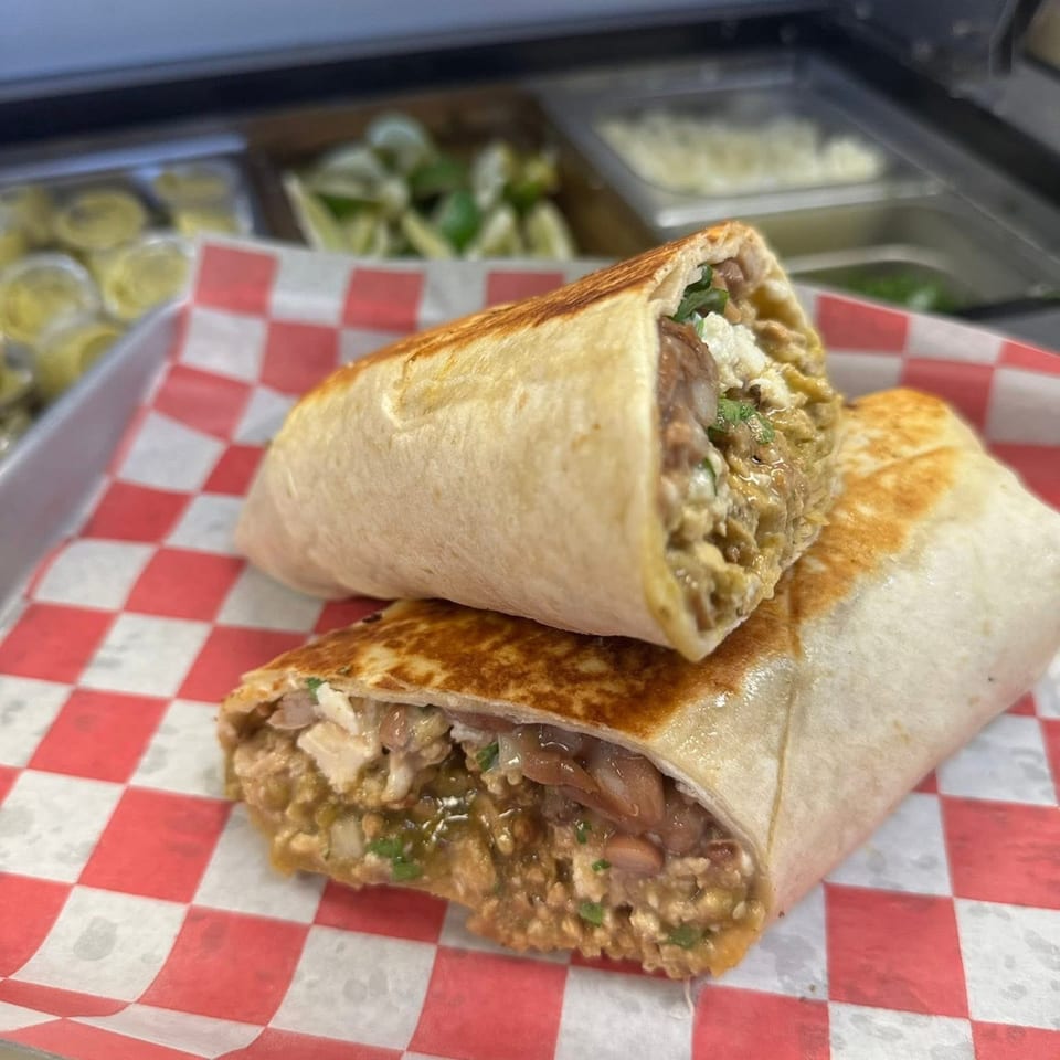 Two halves of a Cali Burrito, filled with meat, beans, and cheese, on red and white checkered paper.