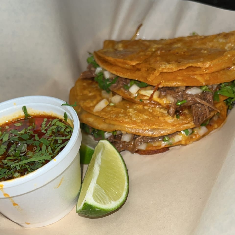 Three Cali Burrito birria tacos with cilantro and onions, served with consommé and lime.