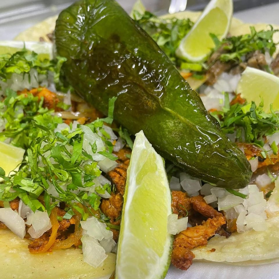 Close-up of Cali Burrito Mexican Grill's tacos, topped with cilantro, onions, lime, and a large green pepper.