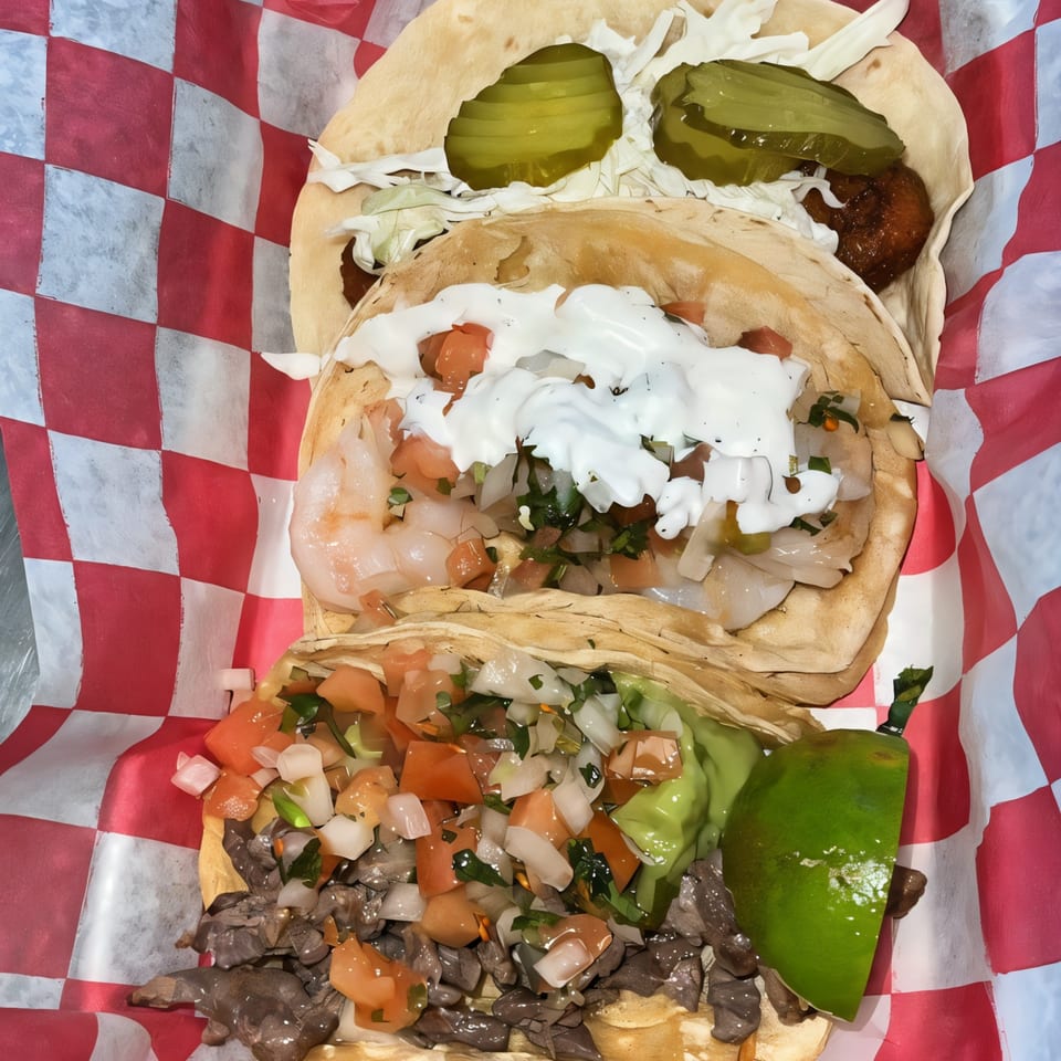 Three Cali Burrito Mexican Grill tacos, including shrimp, steak, and a fried option, in a red checkered basket.