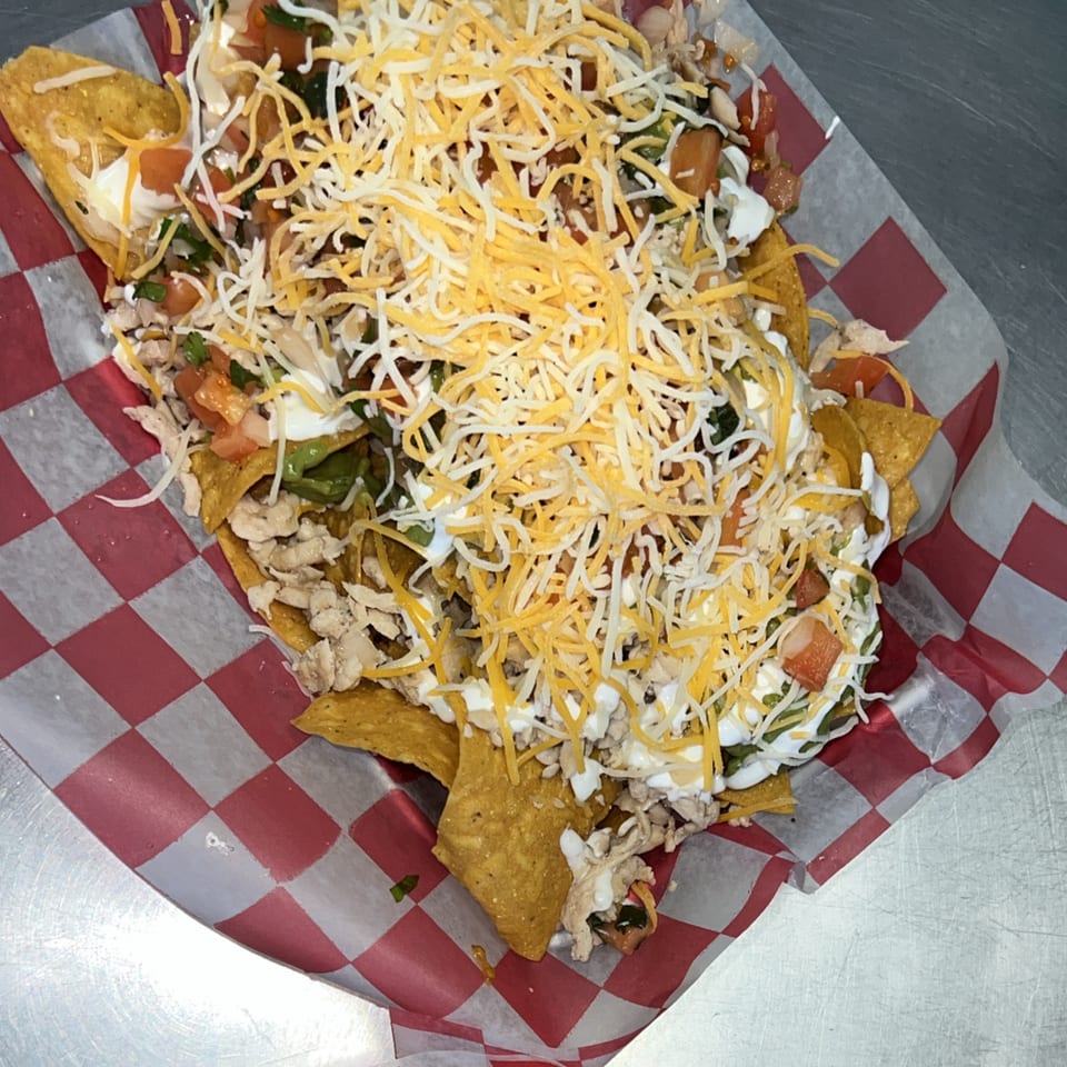 Loaded nachos with chicken, cheese, sour cream, and pico de gallo in a red checkered basket.