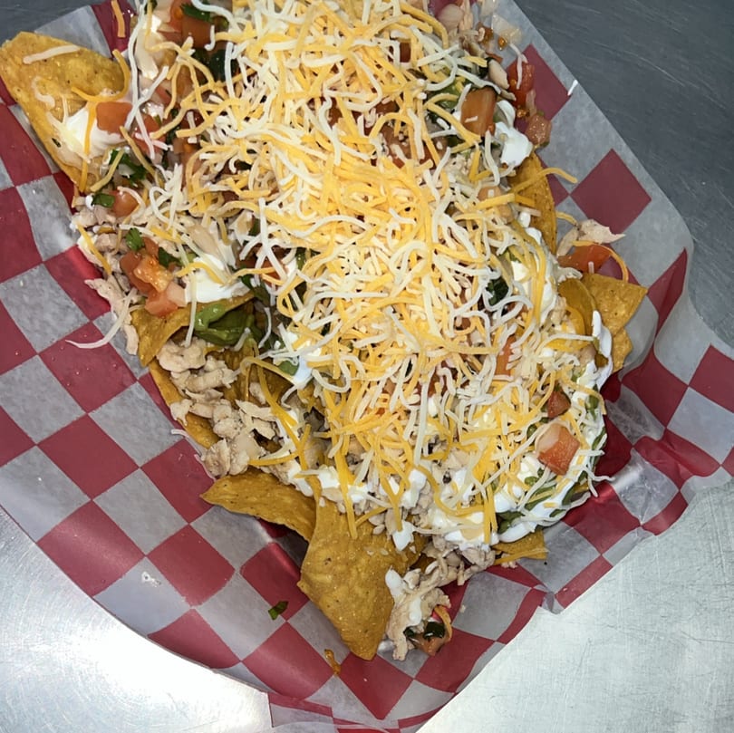 Loaded nachos with chicken, cheese, sour cream, and pico de gallo in a red checkered basket.
