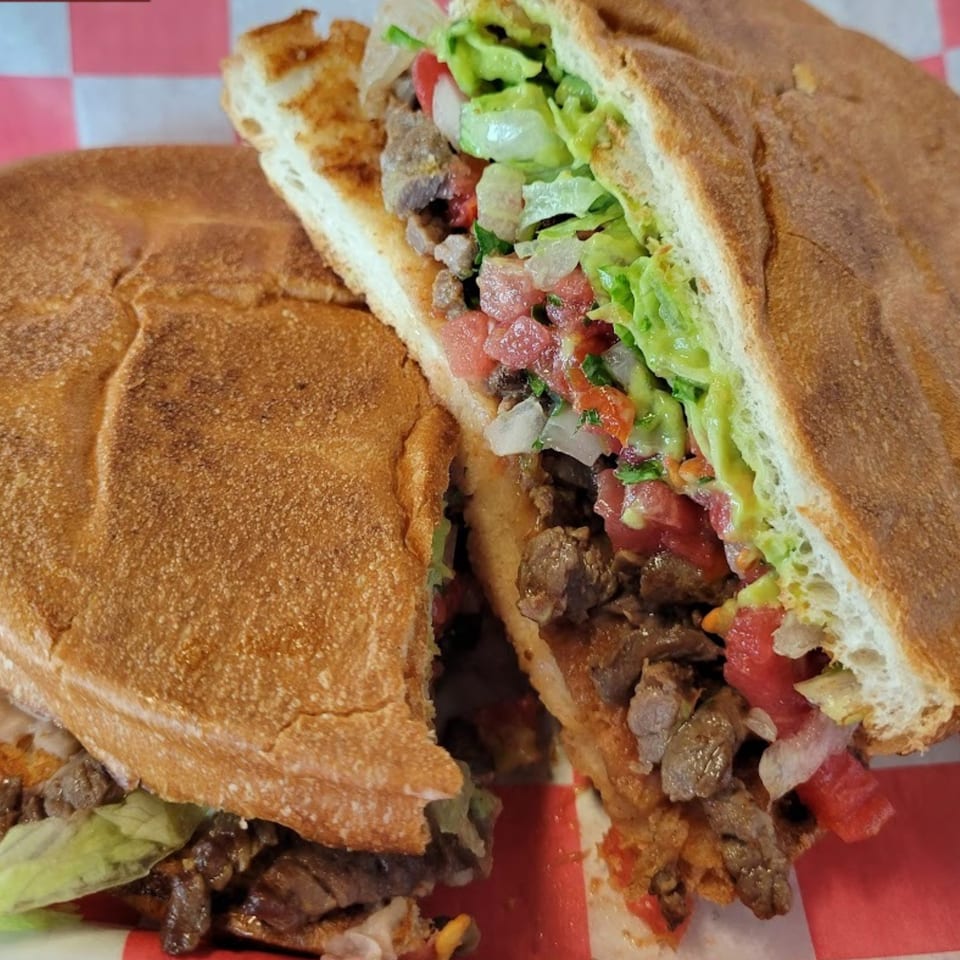 A Cali Burrito Mexican Grill torta, cut in half, revealing steak, lettuce, tomato, and onion.